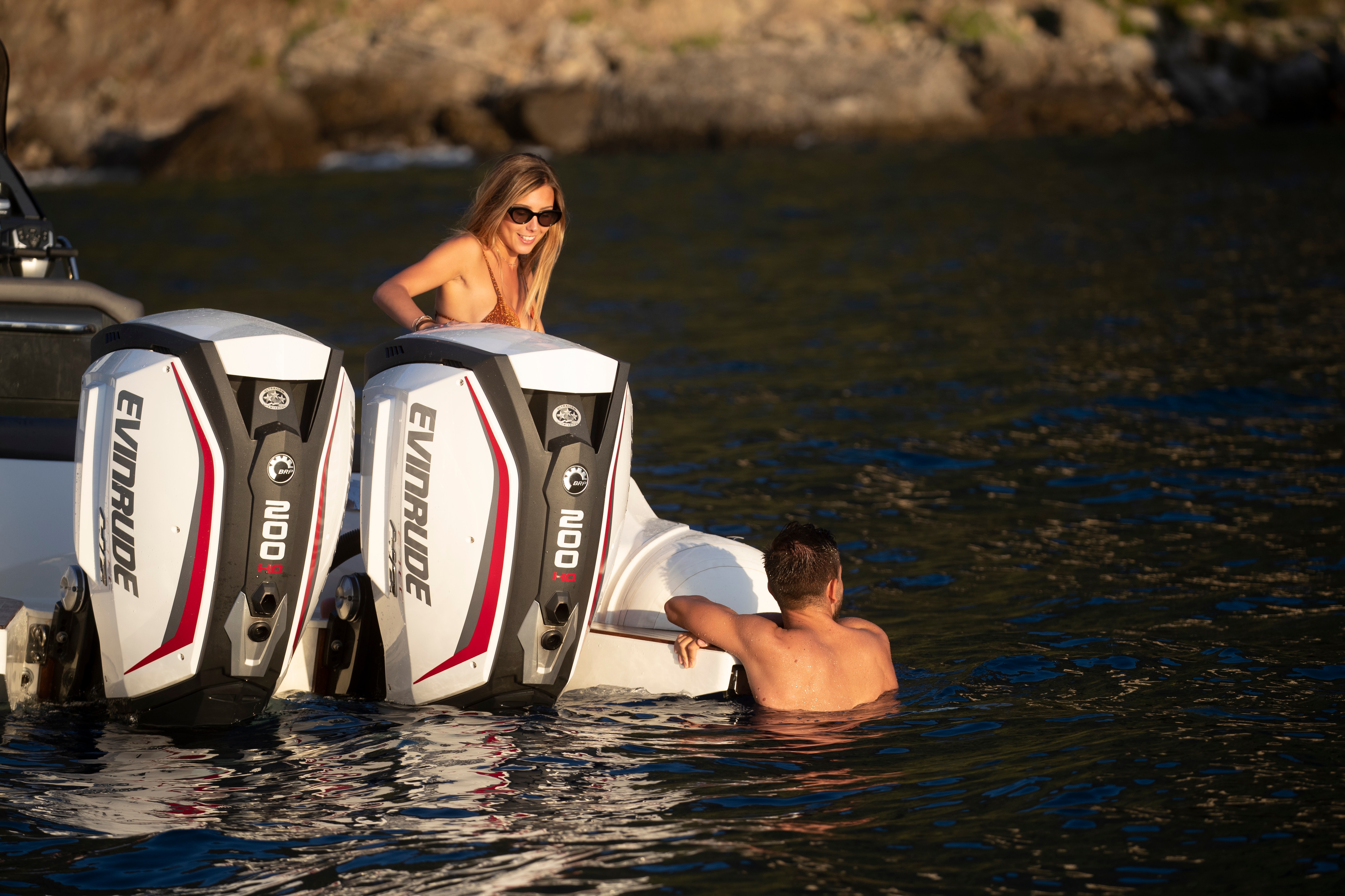 A man and a woman swimming close to a boat yielding an Evinrude motor
