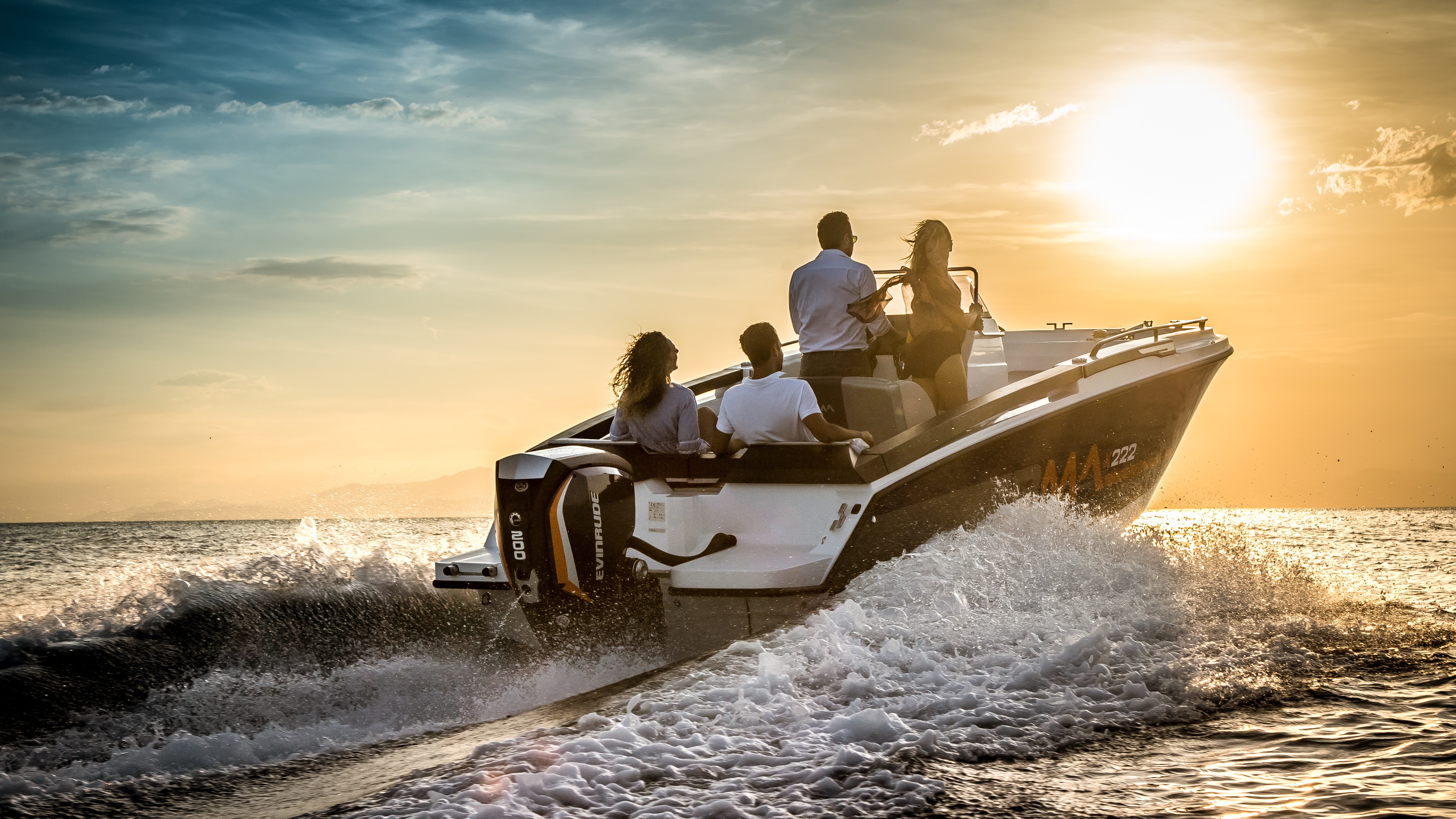 Four people on a boat yielding an Evinrude motor driving towards the sunset