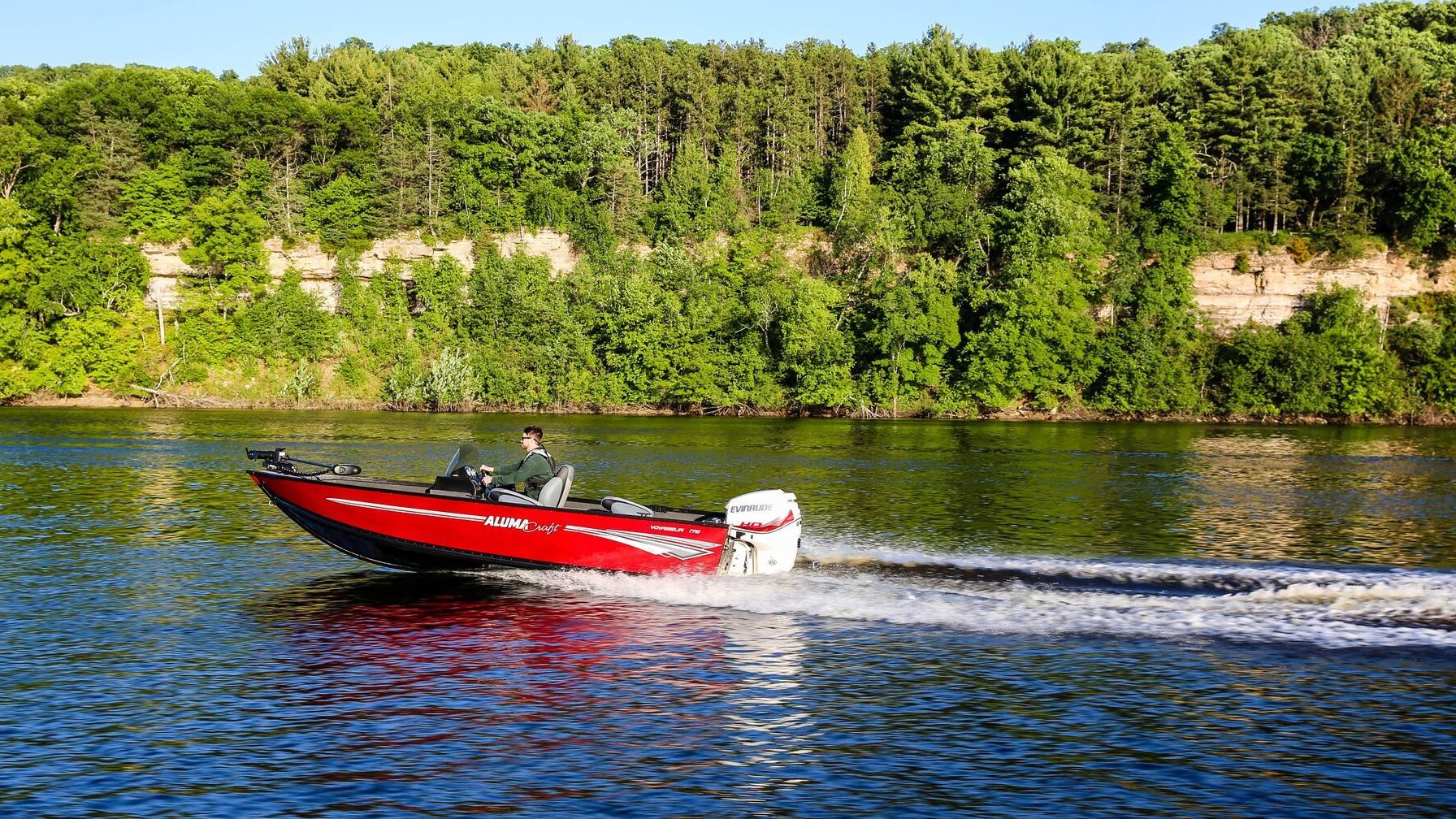 Man driving his Alumacraft boat with an Evinrude motor in a lake