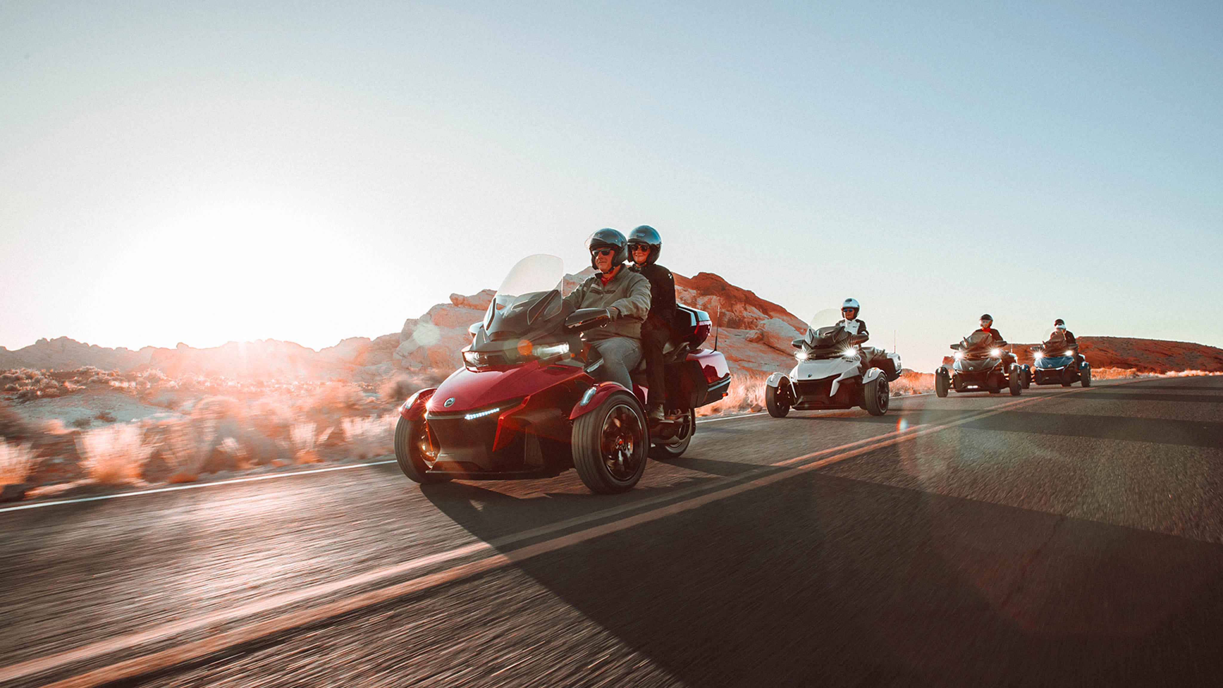 Group of people riding four Can-Am Ryker vehicles on a scenic road