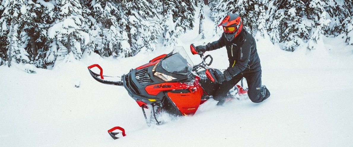  Čovjek koji lebdi sa svojim motornim sanjkama Expedition klečeći na snijegu