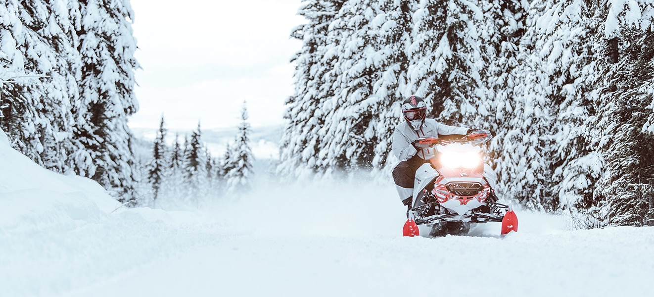 Muž jedoucí na skútru Ski-Doo Backcountry zasněženou lesní cestou