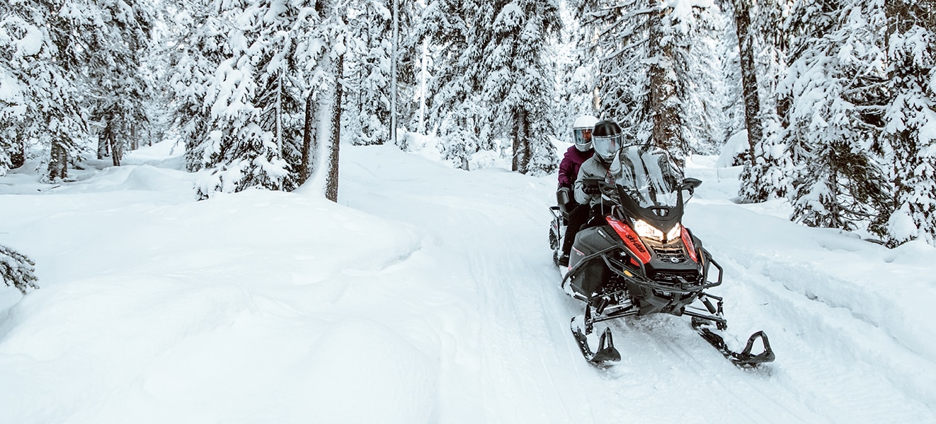 A couple driving a Ski-Doo Expedition through a snowy forest trail
