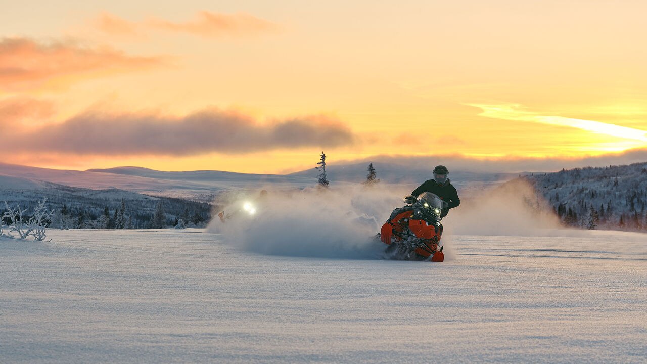 Two 2026 Lynx Brutal RE snowmobiles carving through deep snow at sunset