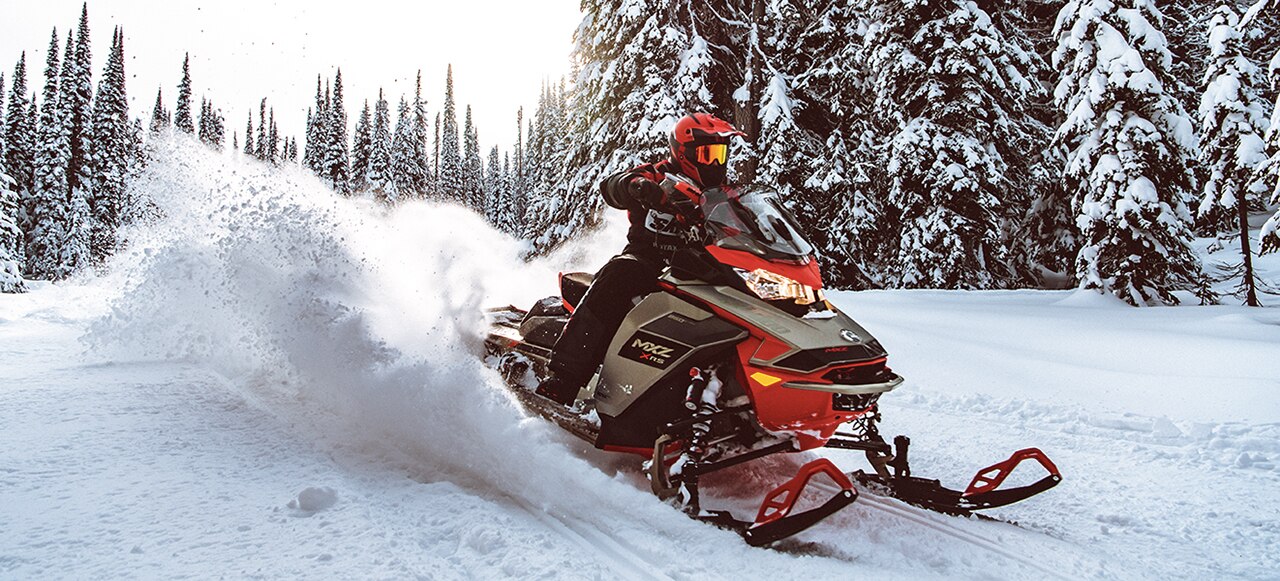 Mann, der einen Ski-Doo MXZ durch einen verschneiten Wald fährt