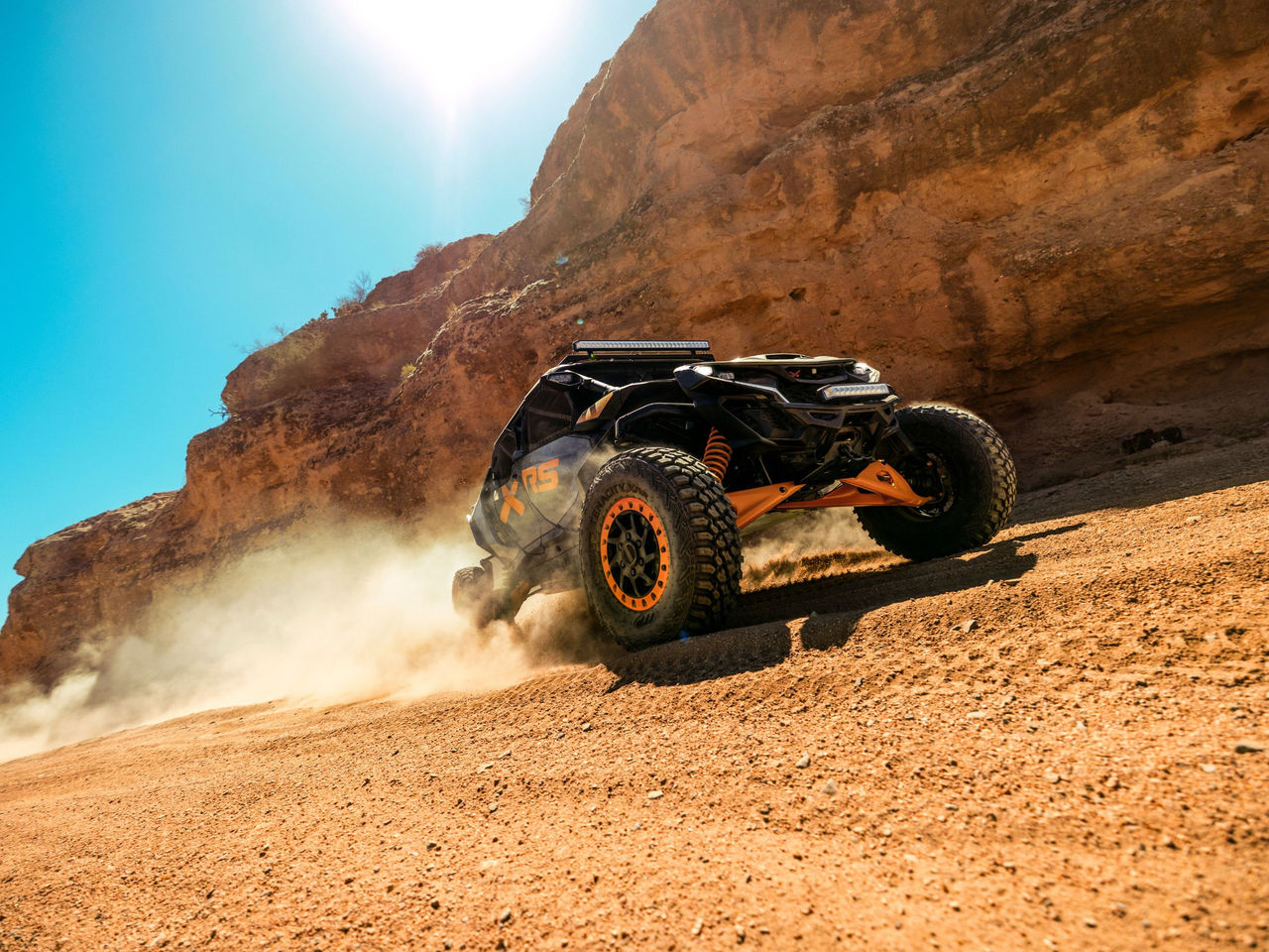2027 Can-Am Maverick MAX X-RS riding in the sand next to a wall of rocks