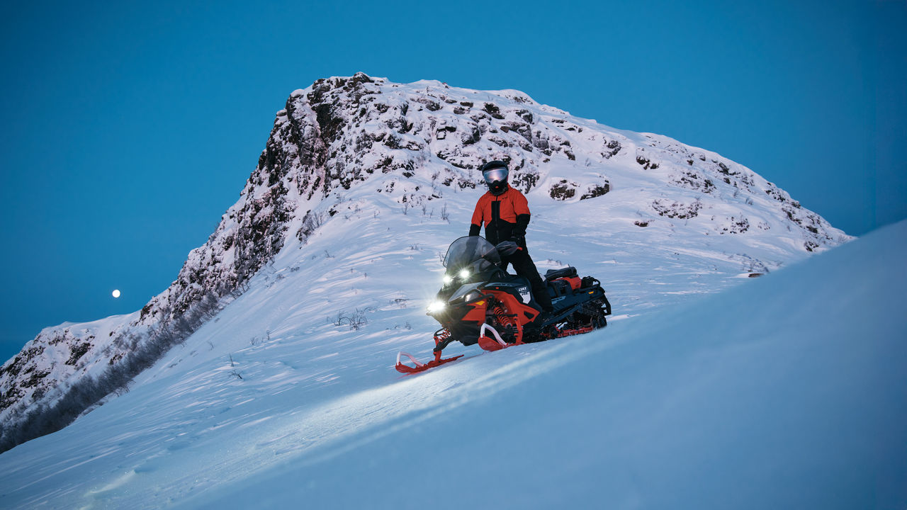 Rider standing on a 2027 Lynx Brutal snowmobile atop a mountain