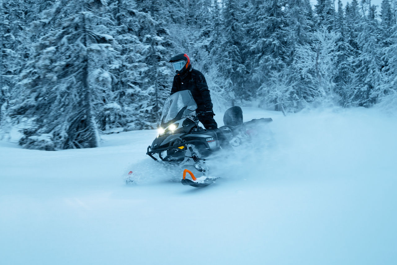 Rider snowmobiling through a snowy forest on a 2027 Lynx 59 Ranger snowmobile