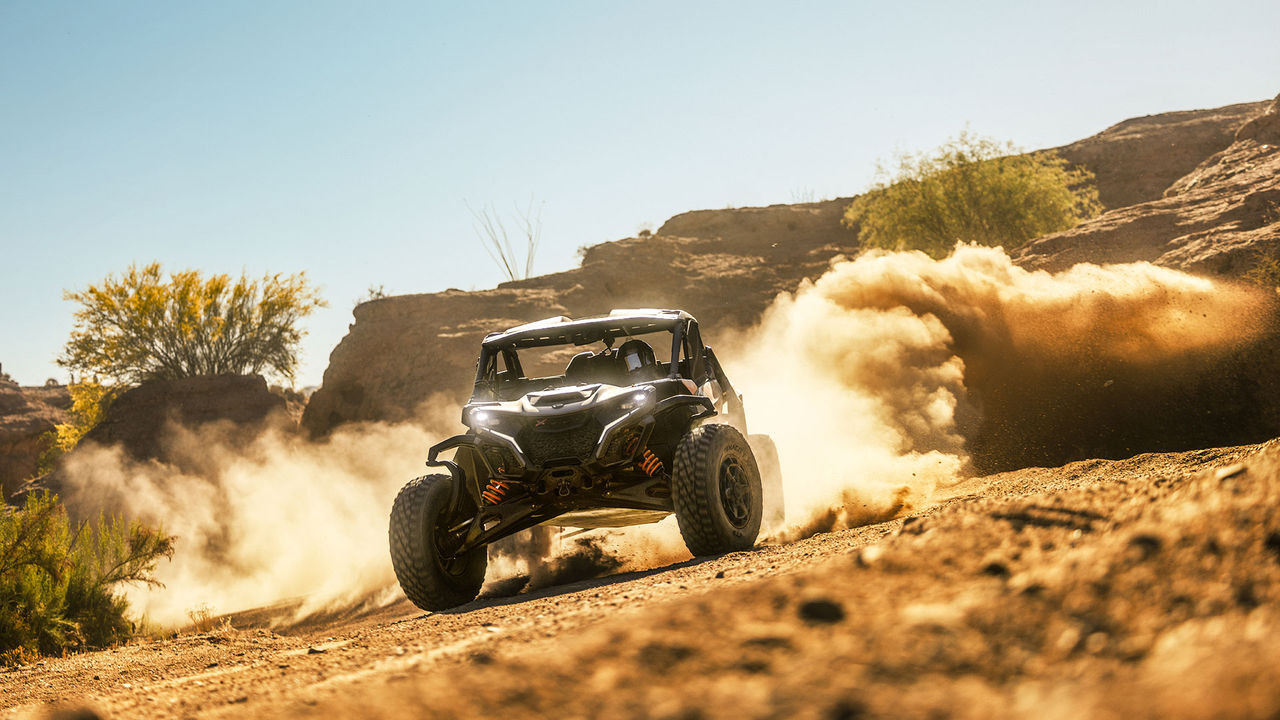 A Can-Am Maverick X RS side-by-side vehicle riding in the desert, leaving a cloud of dust behind