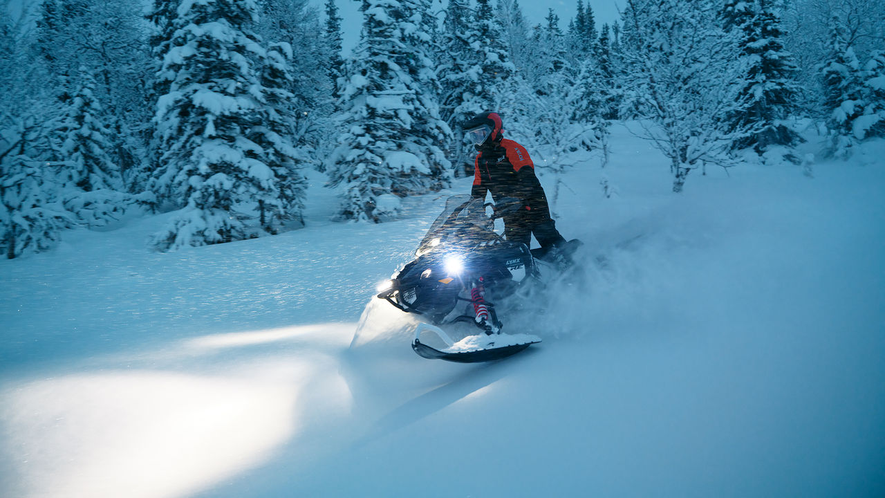 Rider riding a 2027 Lynx Commander RE in a snowy forest at dusk