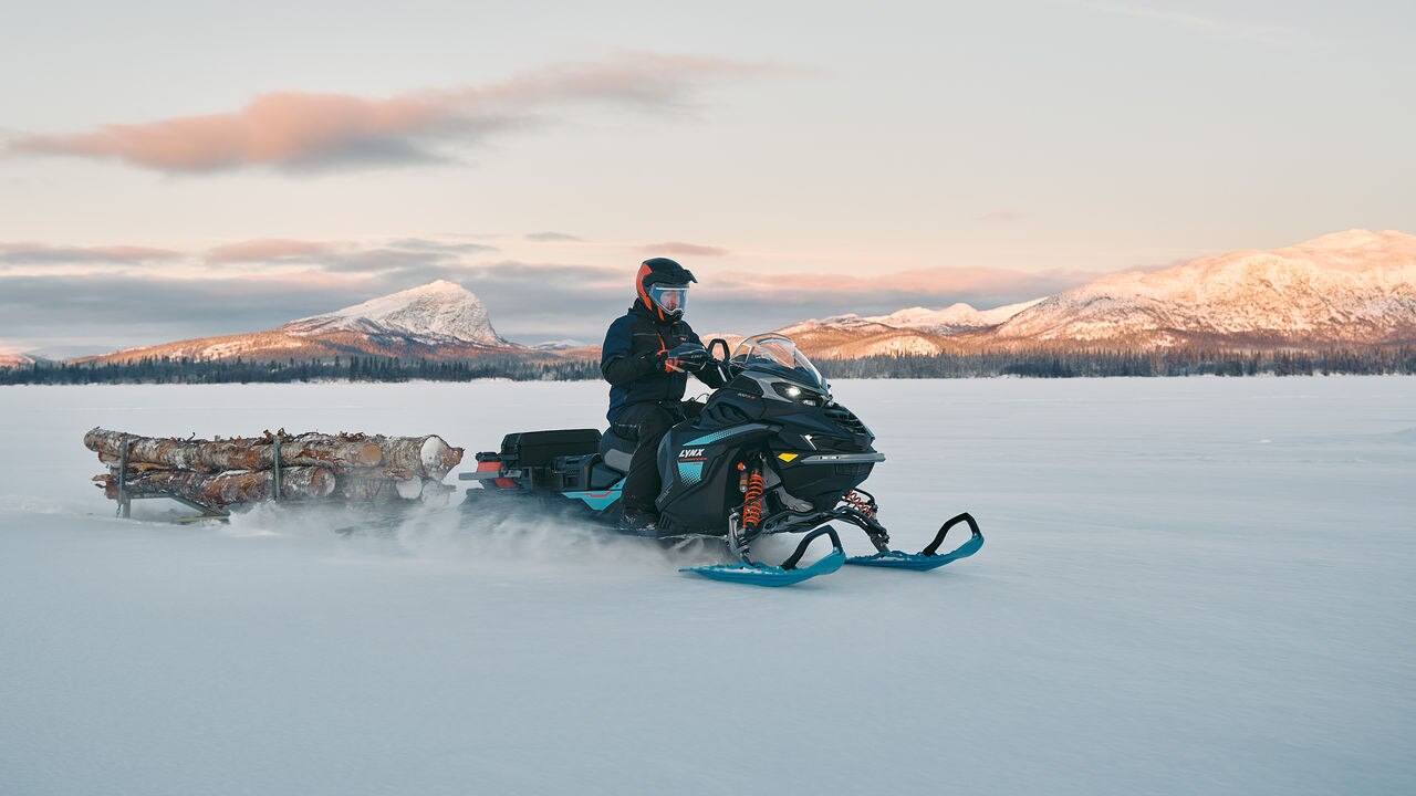 2026 Lynx Commander RE snowmobile towing a load of timber in a sleigh on a frozen lake.