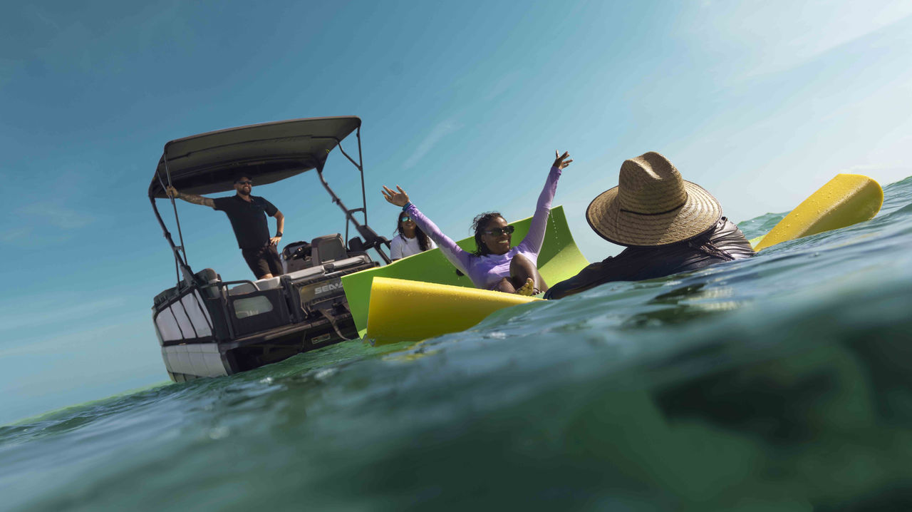 A women enjoying the water on a flotting mat behind a Sea-Doo pontoon