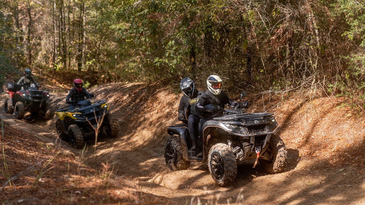 Three Outlander ATVs on a bumpy trail in the forest