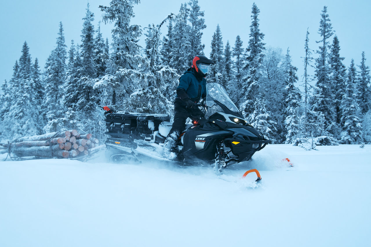 Man riding a 2027 Lynx 69 Ranger PRO snowmobile while log hauling