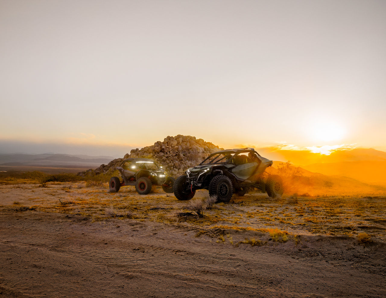 Two Can-Am Maverick side-by-side in the desert with a sunset