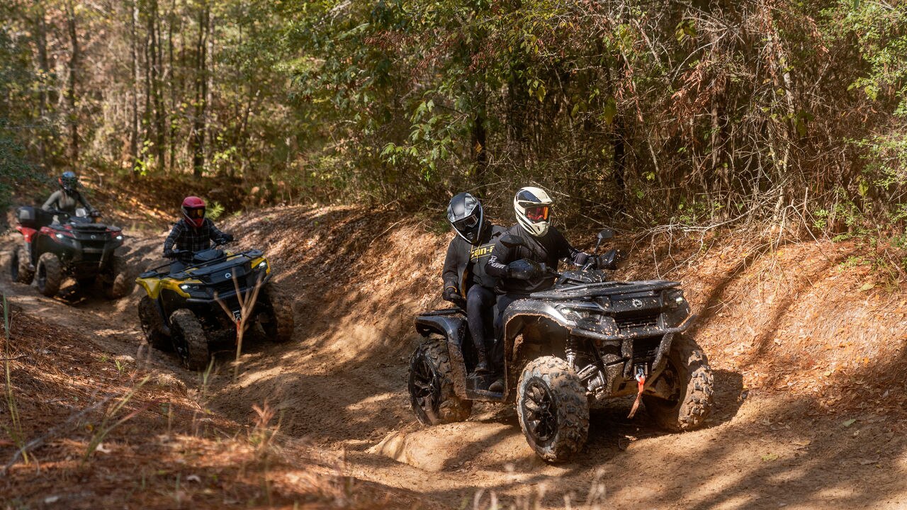 Three Outlander ATVs on a bumpy trail in the forest