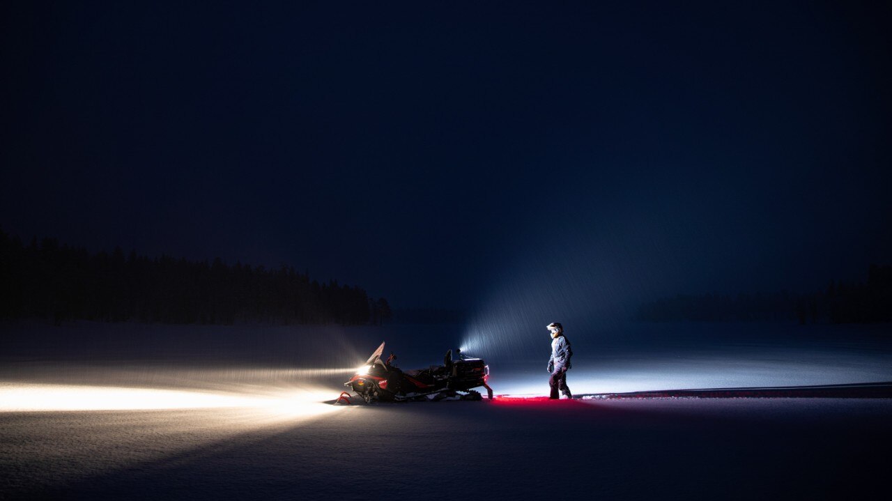  Široki snimak muškarca koji noću ide prema svojim motornim sanjkama Lynx 2021