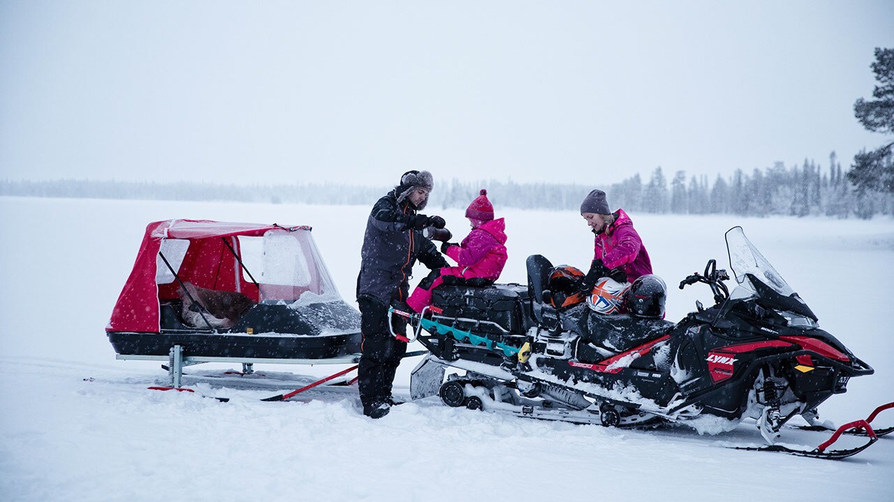 A man and a woman are installing a little girl in the back of a 2021 Lynx 59 Ranger Model which is equipped with a rear trailer.