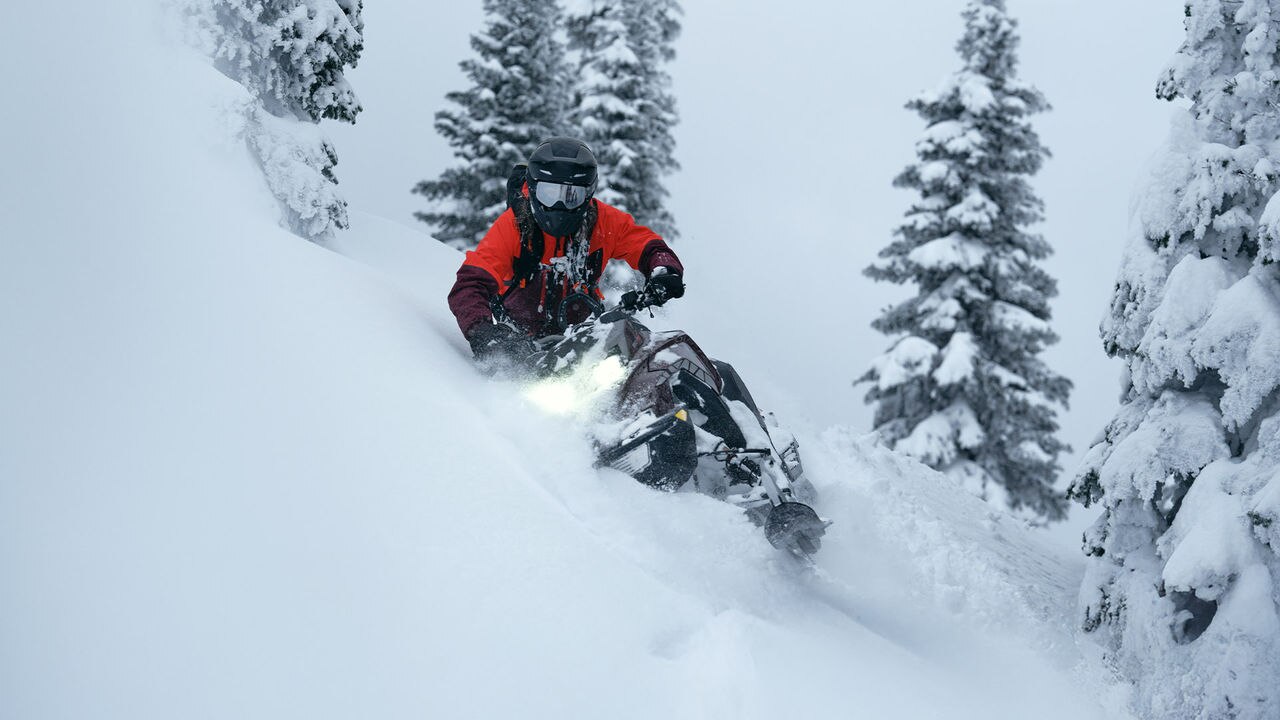 Man riding a Ski-Doo snowmobile down a snowy mountain