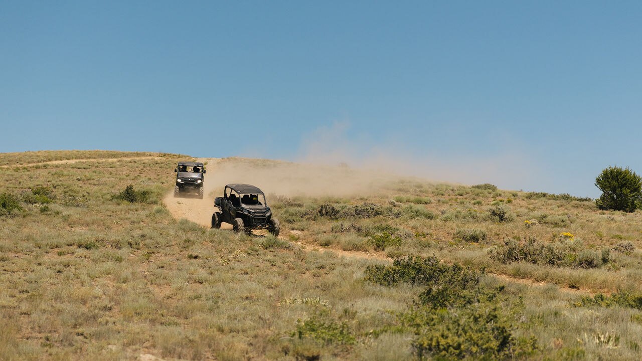 Two Can-Am Side-by-side (SxS) vehicle riding on a dirt road