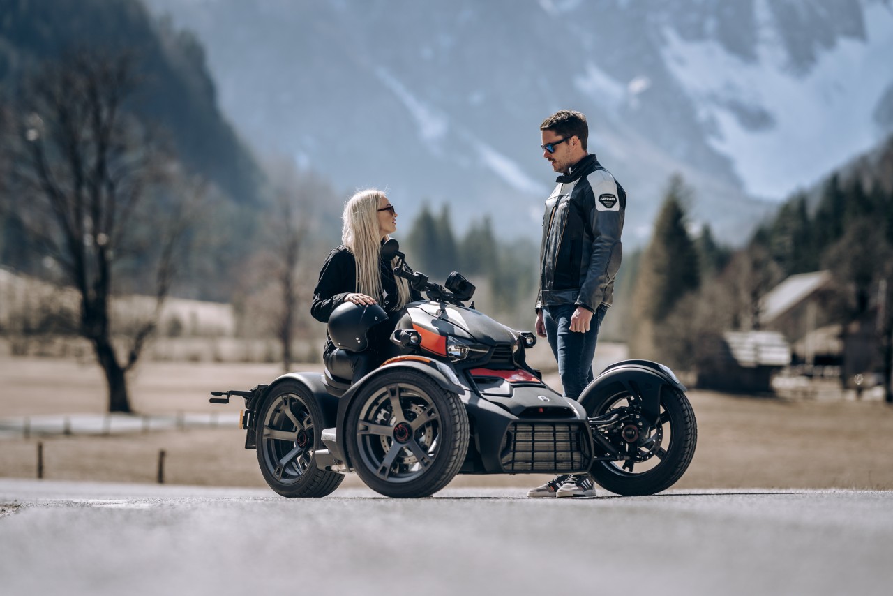 A man and a woman riding Can-Am Spyder 2021 near the lake