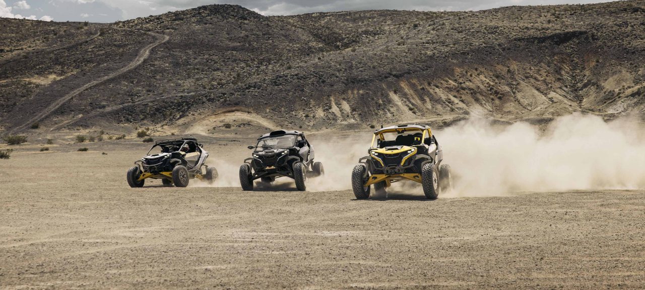 Three Can-Am Maverick R SxS vehicles racing through the desert