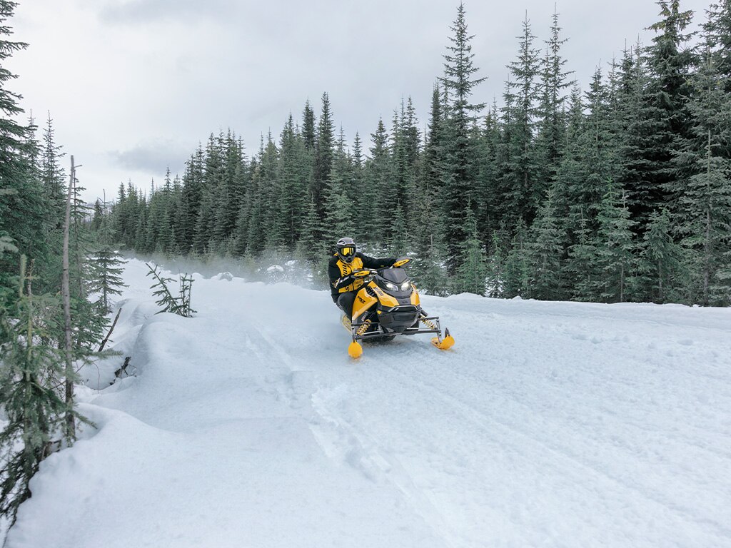 Rider going at high speed with a 2027 Ski-Doo MXZ RS snowmobile on a snowy trail surrounded by trees