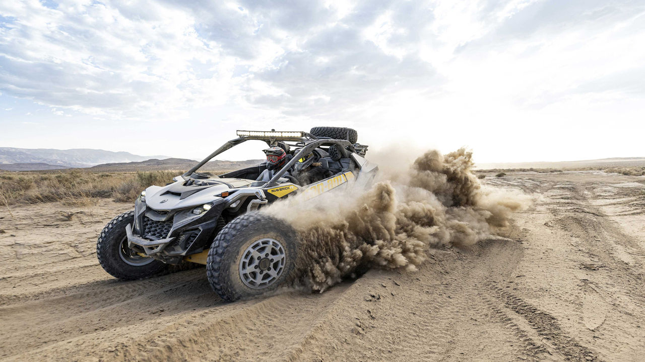 Two riders in a Can-Am Maverick R SxS vehicle speeding through the desert
