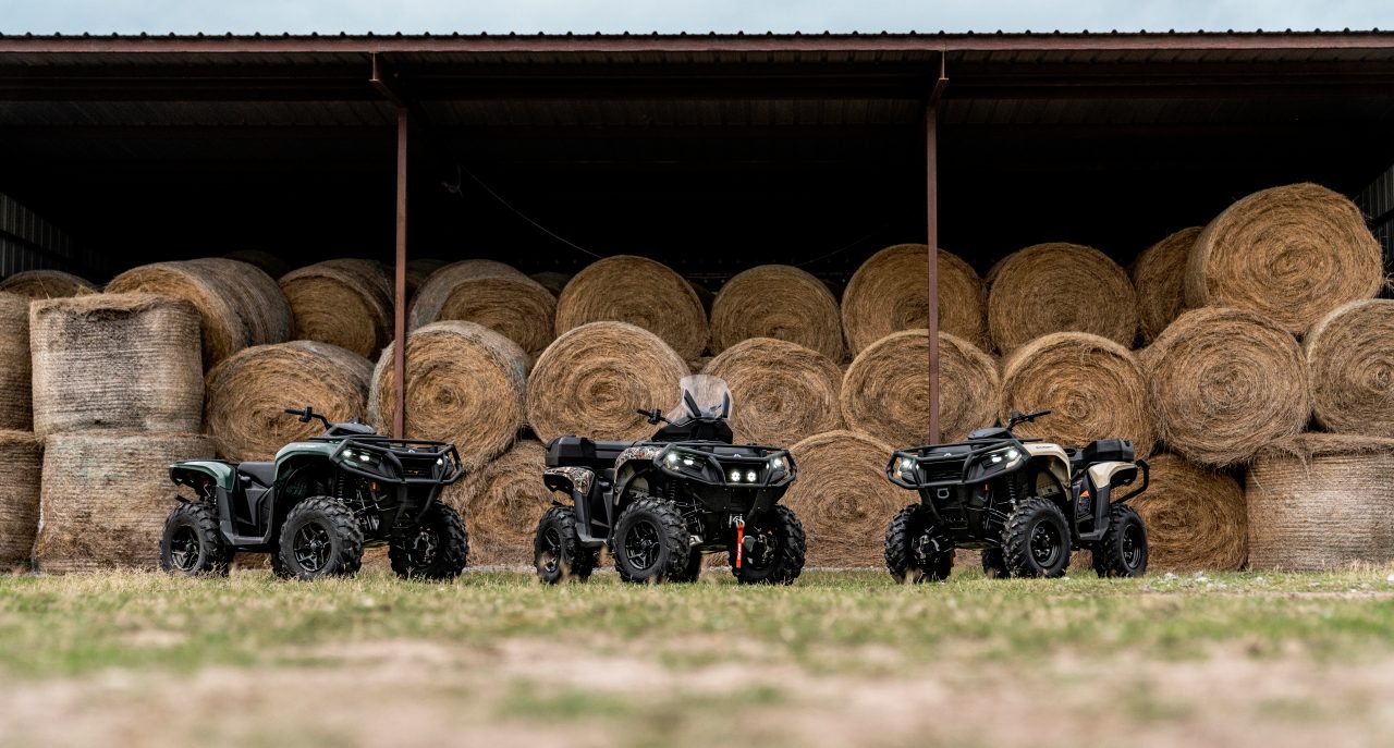 Three Outlanders in a field in front of bales of hay