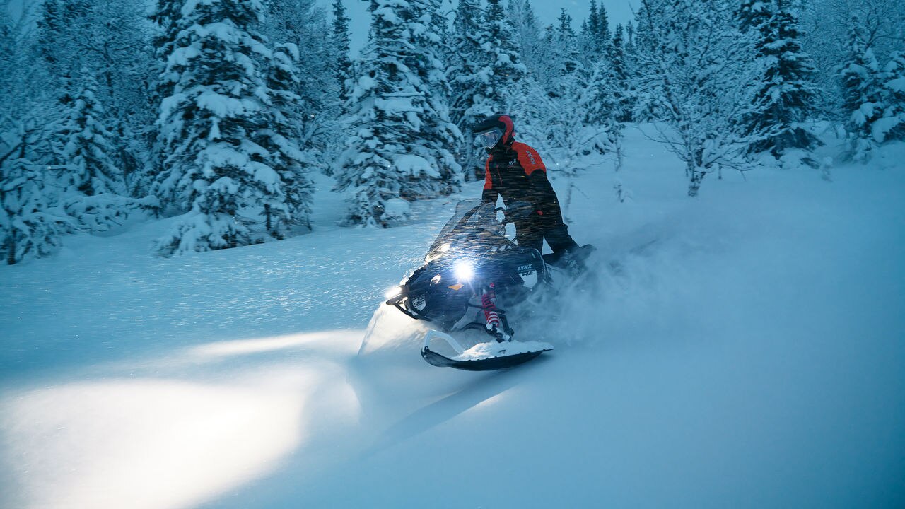Rider riding a 2027 Lynx Commander RE in a snowy forest at dusk