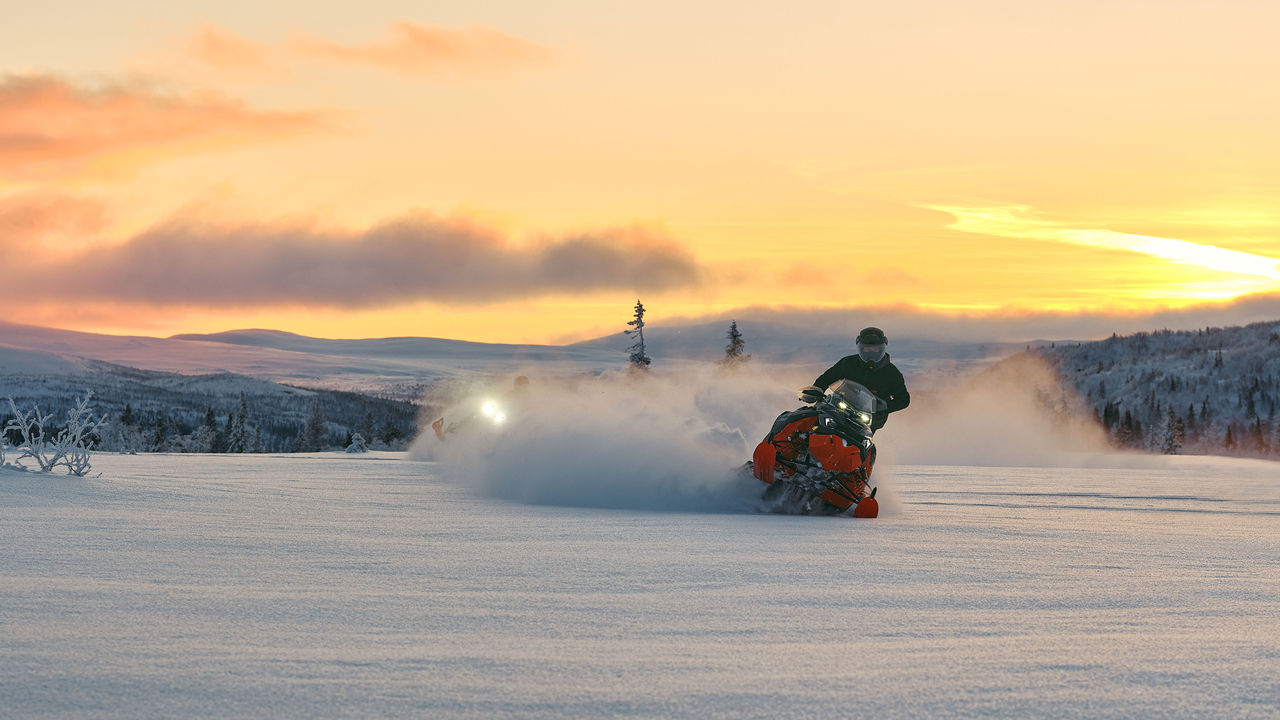 Two 2026 Lynx Brutal RE snowmobiles carving through deep snow at sunset