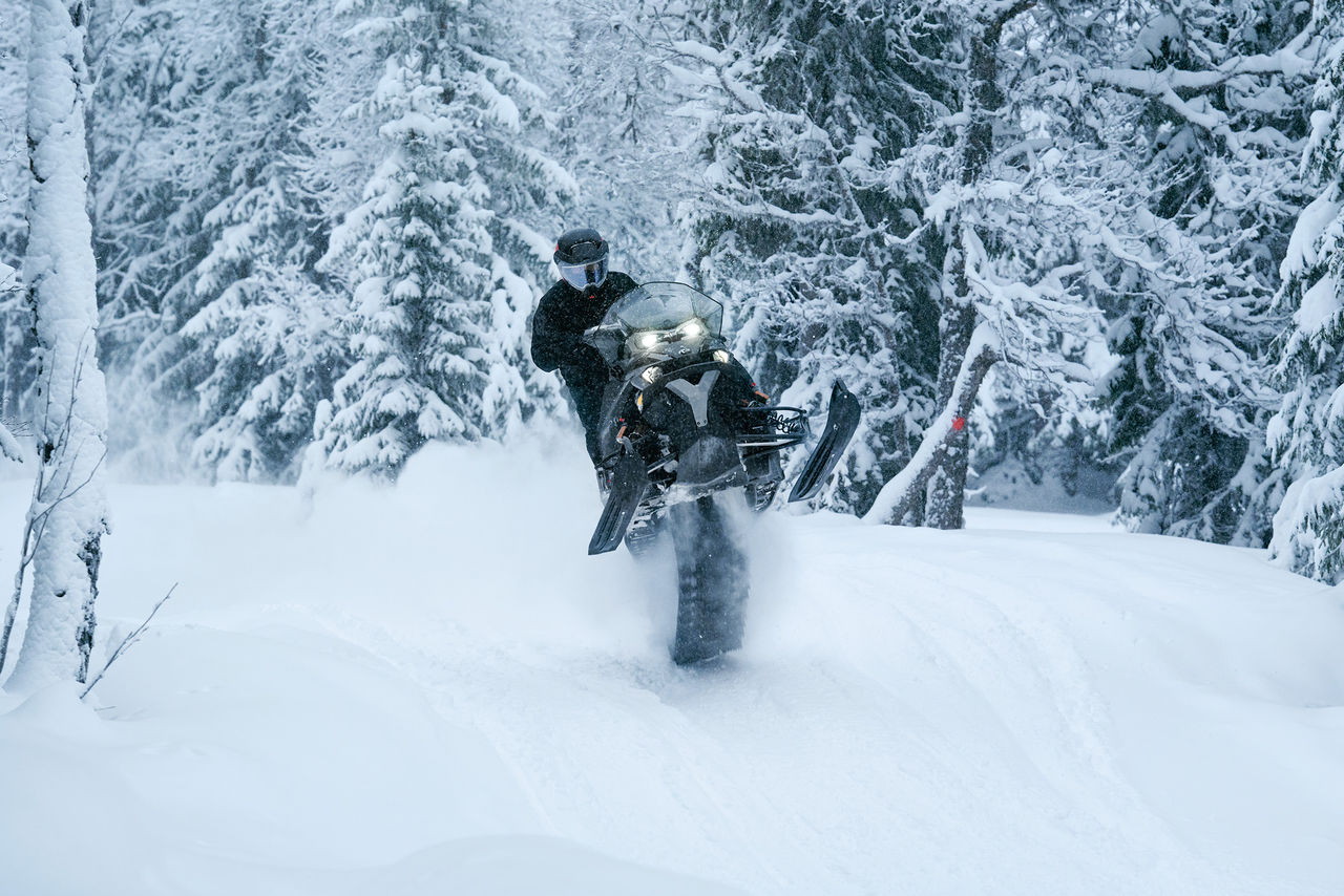 Rider pulling off a jumping stunt on a 2027 Lynx Xterrain snowmobile in a snowy forest