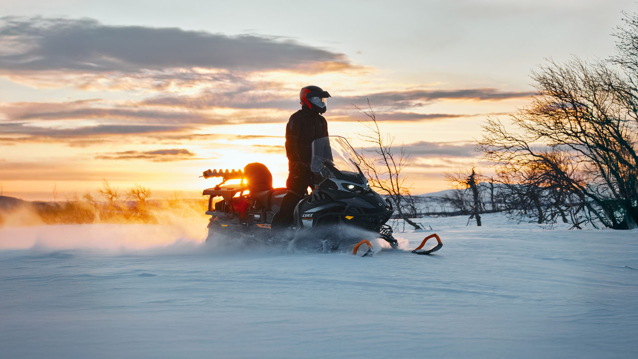 Man standing on his 2027 Lynx 59 Ranger PRO utility snowmobile at dawn