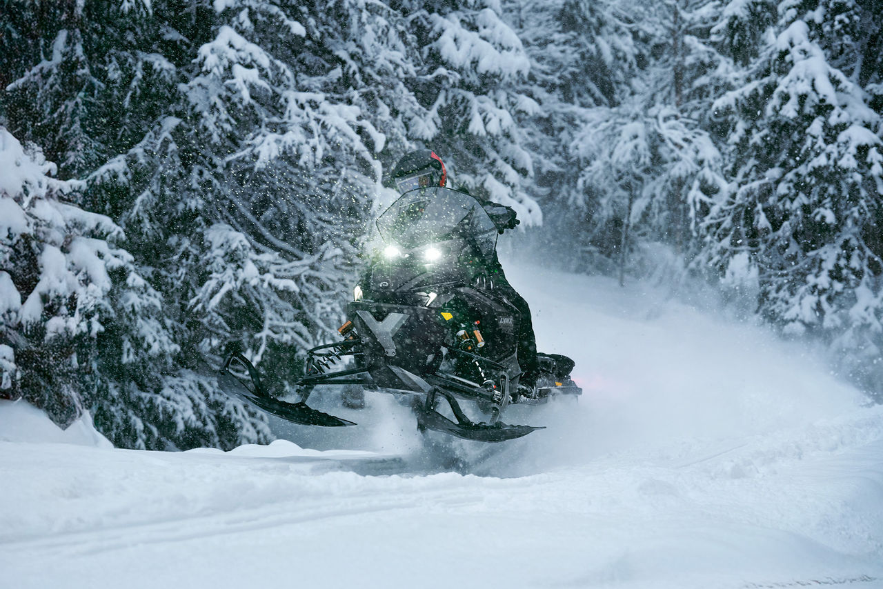 Райдер едет на снегоходе Lynx Xterrain 2027 на высокой скорости по заснеженному лесу
