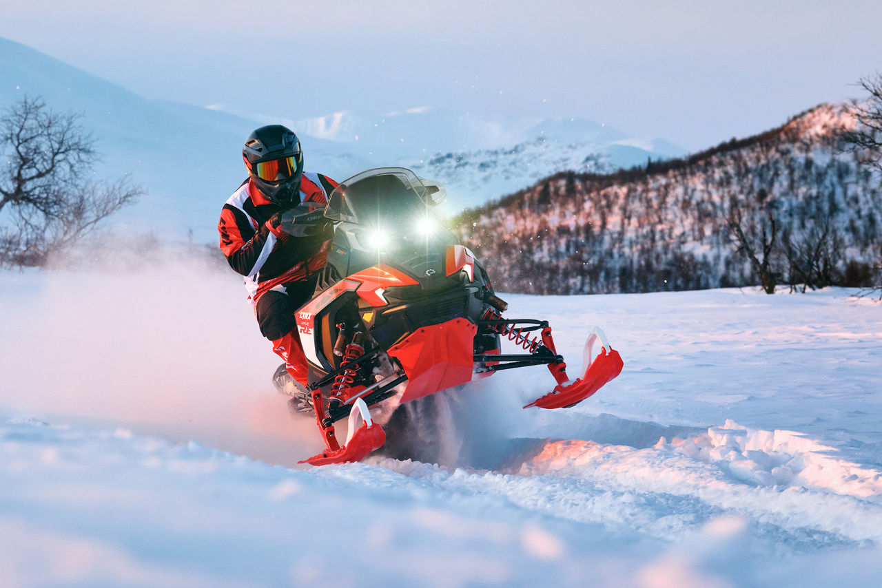 Водитель на снегоходе Lynx Rave RE 2027 едет на высокой скорости по заснеженному полю