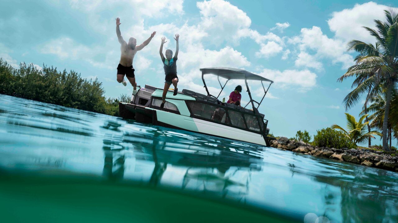 A family jumping into the water near their 2026 Sea-Doo Switch Cruise pontoon boat