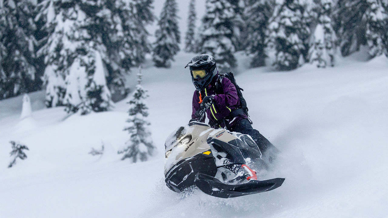 Райдер на снегоходе Ski-Doo Summit 2027 едет по глубокому снегу в горах