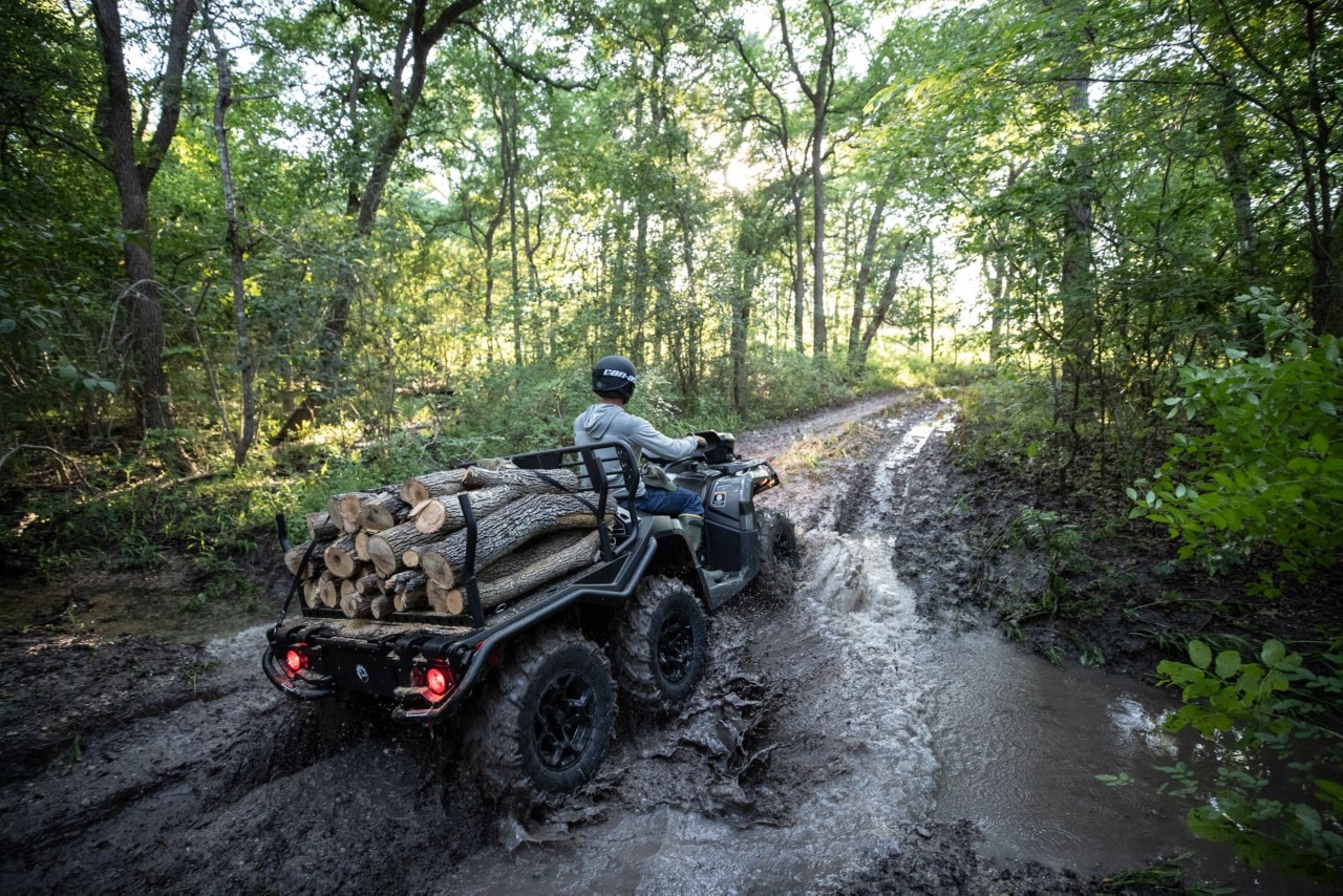 Muž jazdí na Can-Am Outlander 6x6 XT ATV v bahne s drevom na zadnej plošine