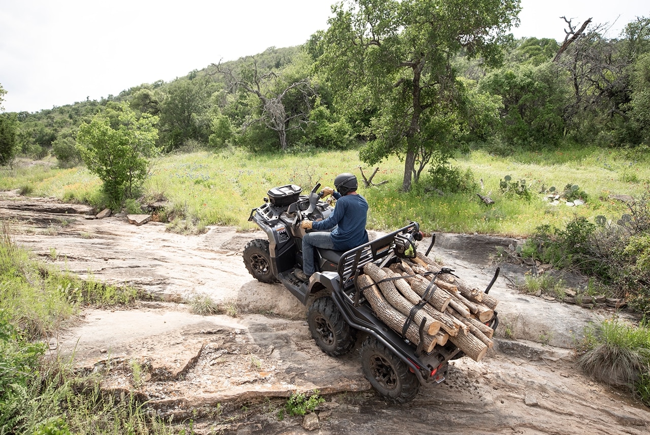 Muž jazdí na Can-Am Outlander 6x6 XT ATV s drevom na zadnej plošine
