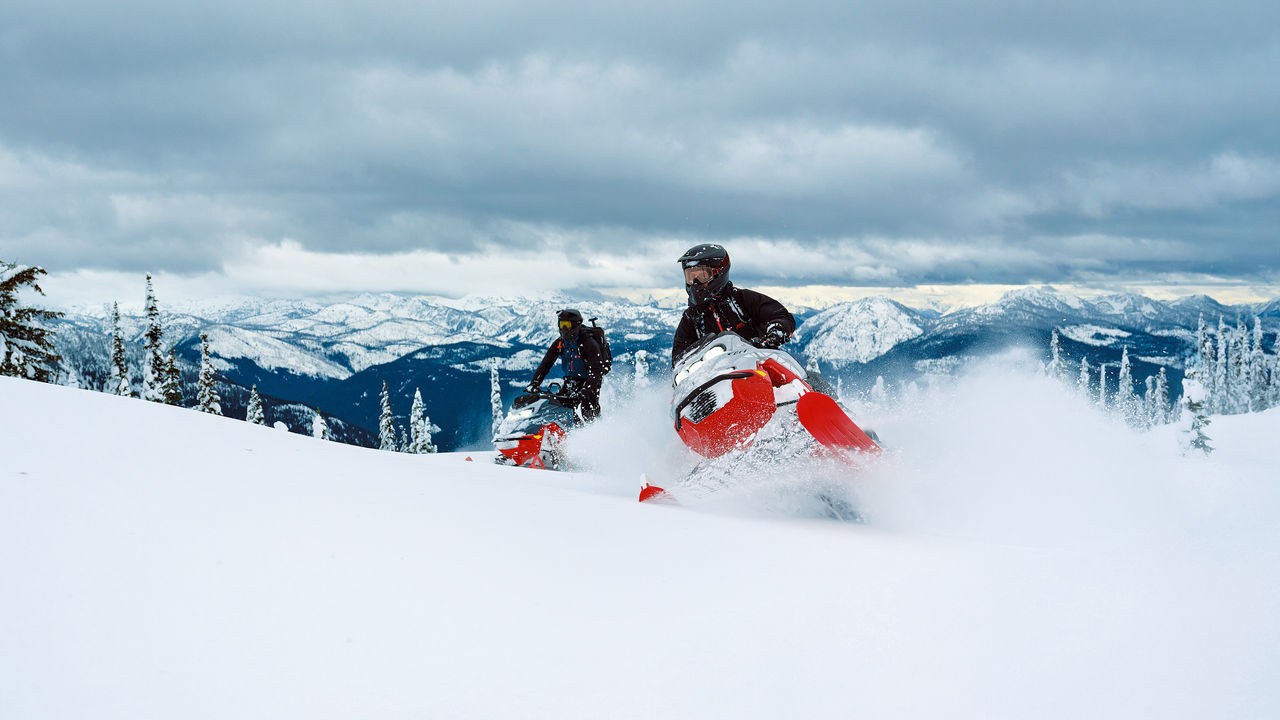 Two 2027 Lynx Shredder DS snowmobile riding up a snowy hill
