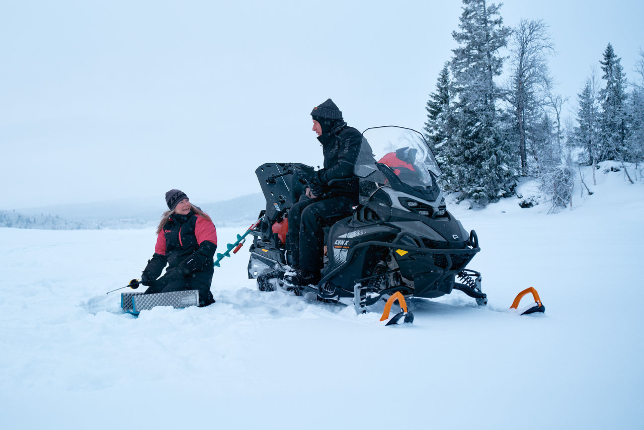 Two people ice fishing next to a 2027 Lynx 59 Ranger