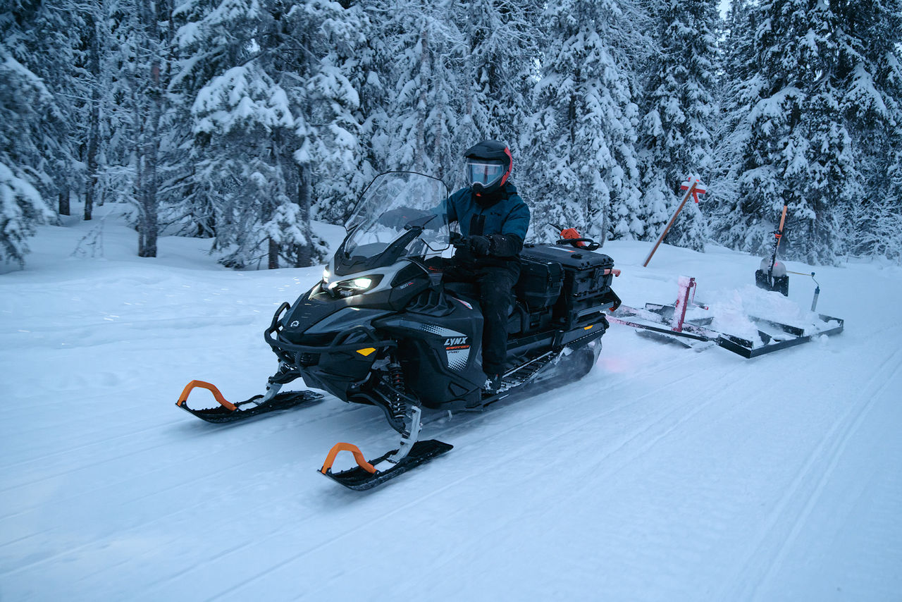 2027 Lynx 69 Ranger riding through a snowy forest pulling a sled
