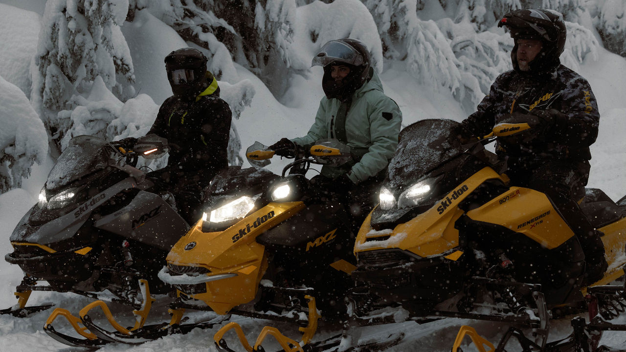 Trije vozniki, ki si oddahnejo od snežne vožnje na svojih motornih saneh Ski-Doo