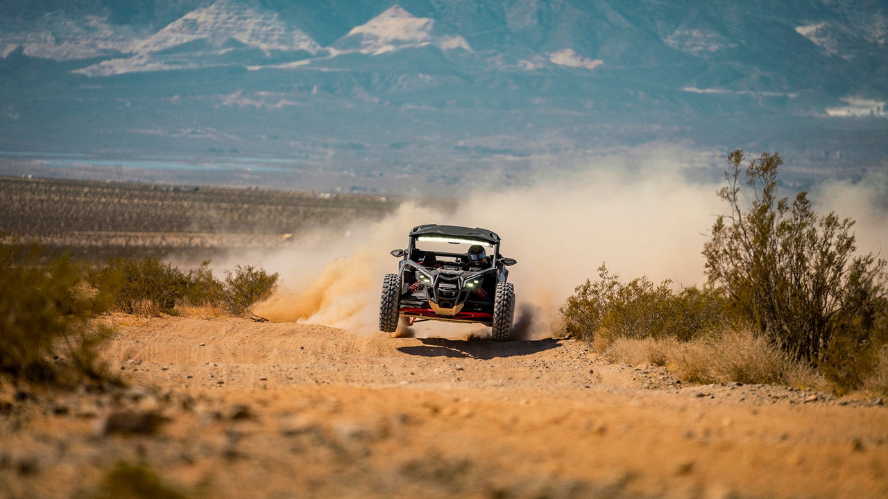 Two riders in a Can-Am Maverick R SxS vehicle speeding through the desert