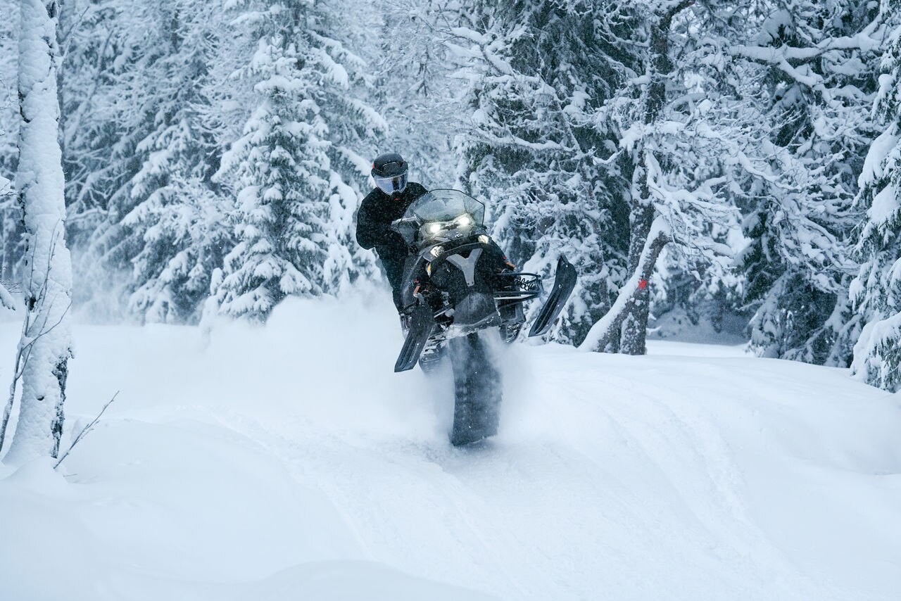 Rider pulling off a jumping stunt on a 2027 Lynx Xterrain snowmobile in a snowy forest