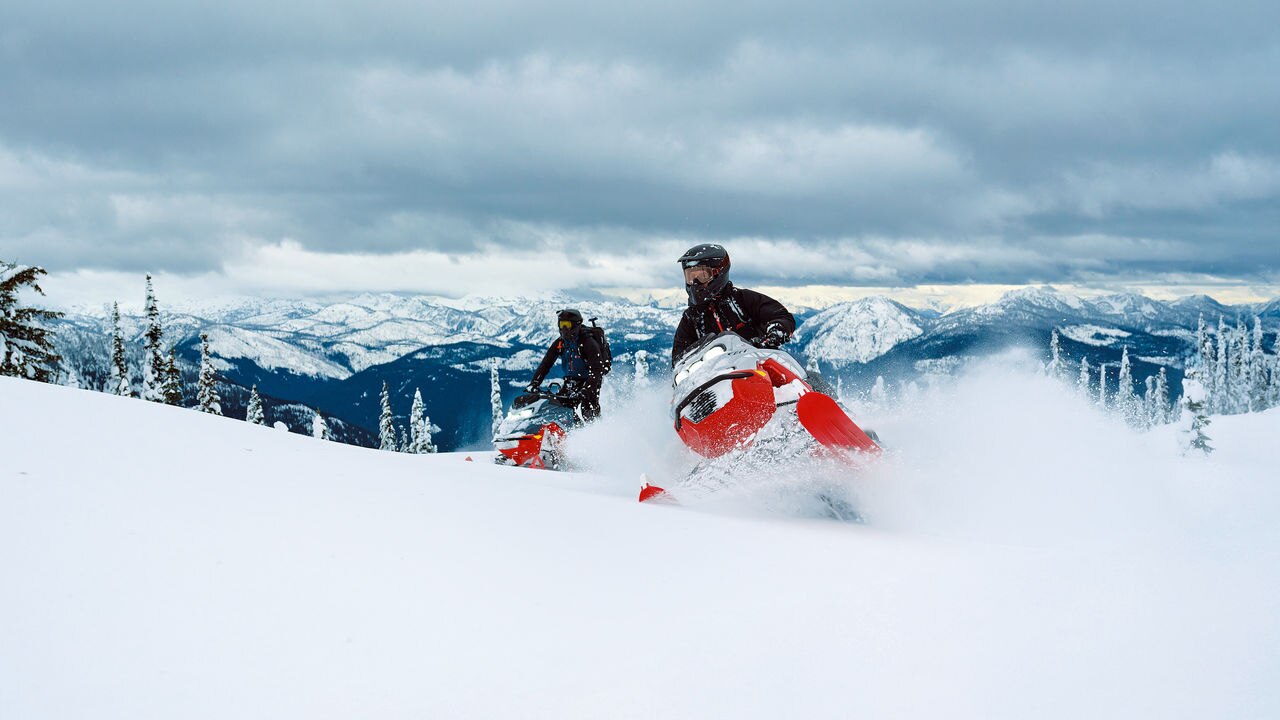 Two 2027 Lynx Shredder DS snowmobile riding up a snowy hill