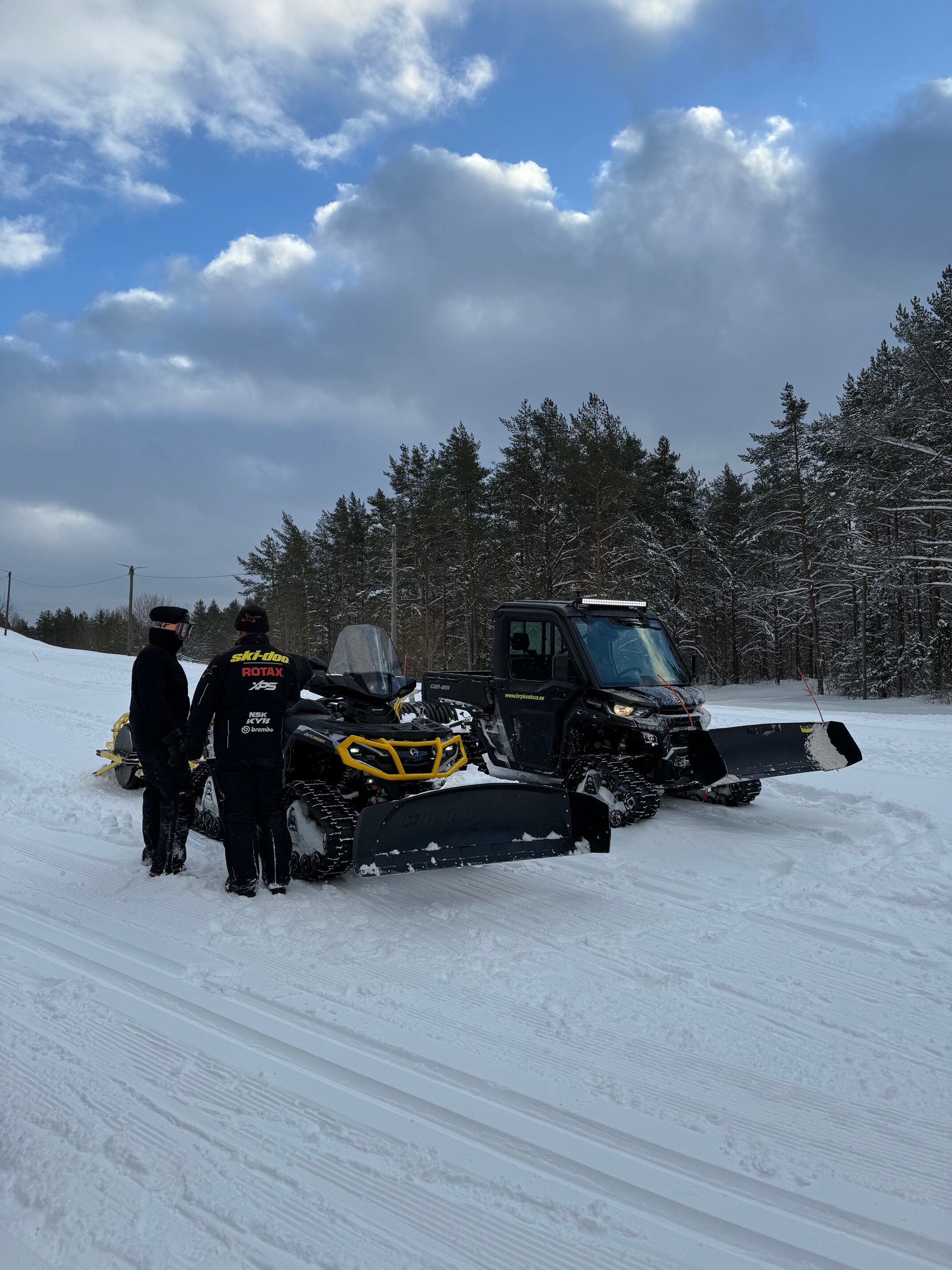 Image of 2 people and 2 vehicles on a snowy path