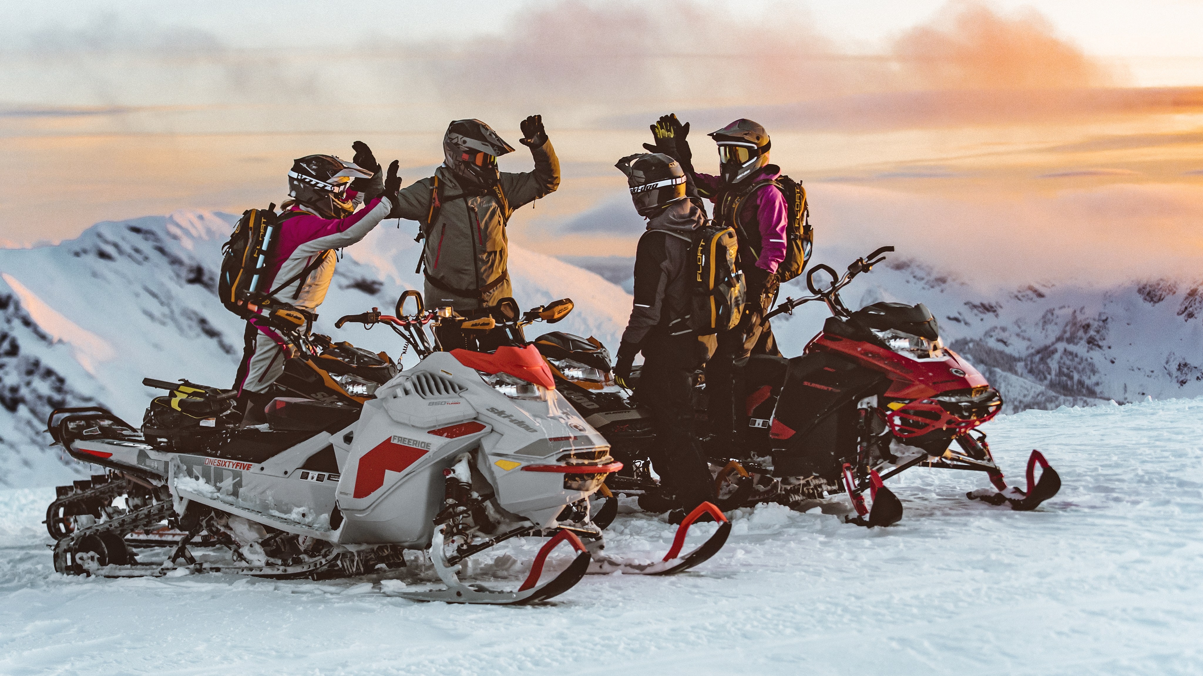 Four friends high fiving near the Ski-doo snowmobiles