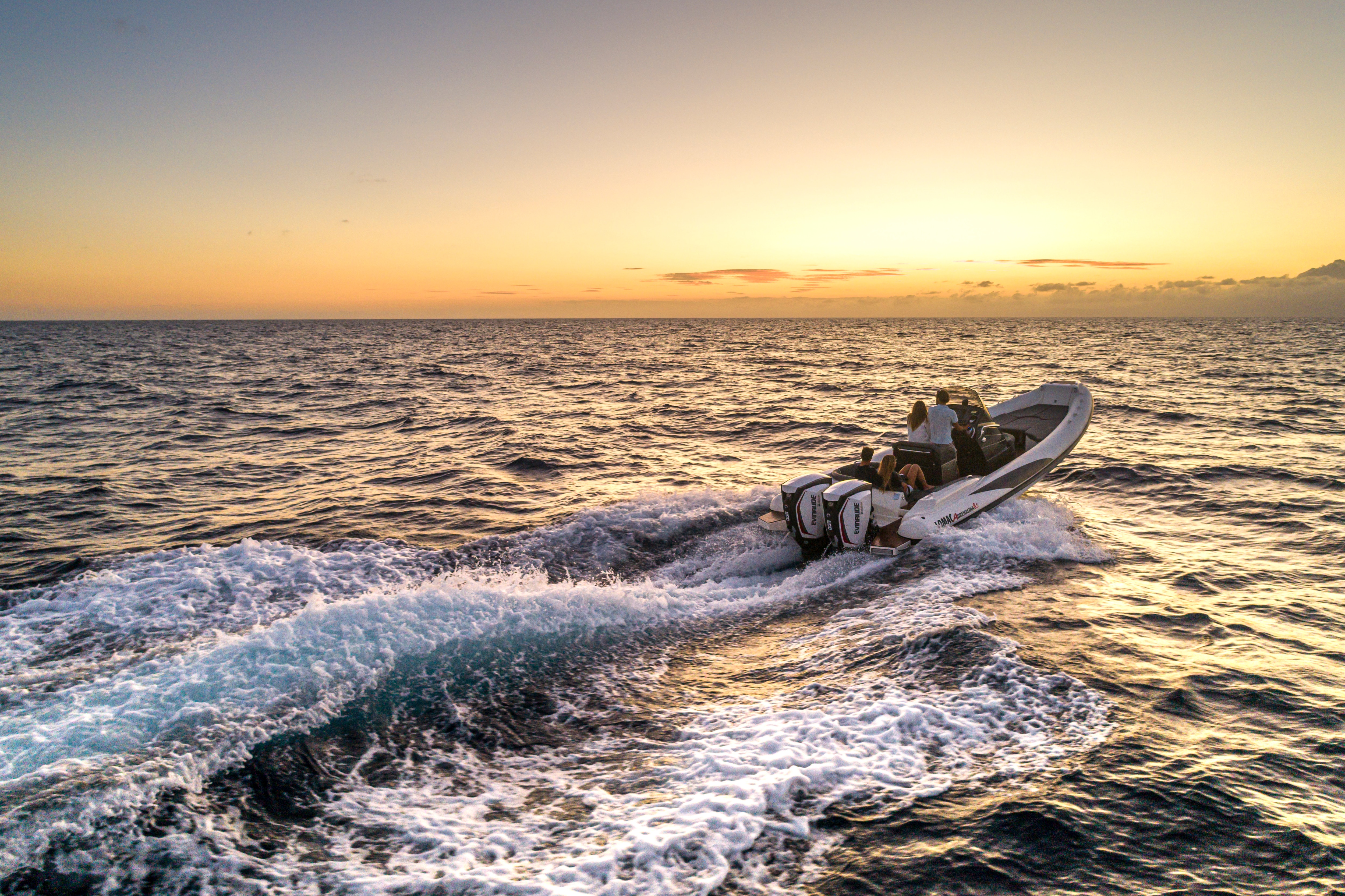 Wide angle shot of a boat yielding an Evinrude motor diving towards the sunset