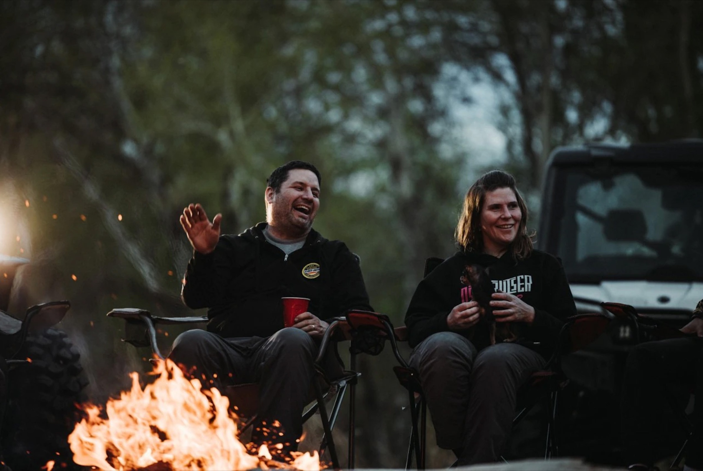 Žena a muž sediaci pri ohni, v pozadí Can-am